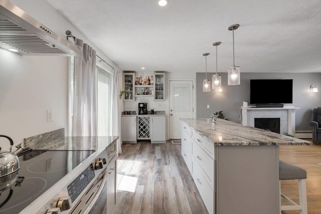 853 Sandwich, Falmouth, MA 02536 - kitchen with stainless steel electric range oven, wall chimney exhaust hood, a breakfast bar, light wood-style flooring, and glass insert cabinets