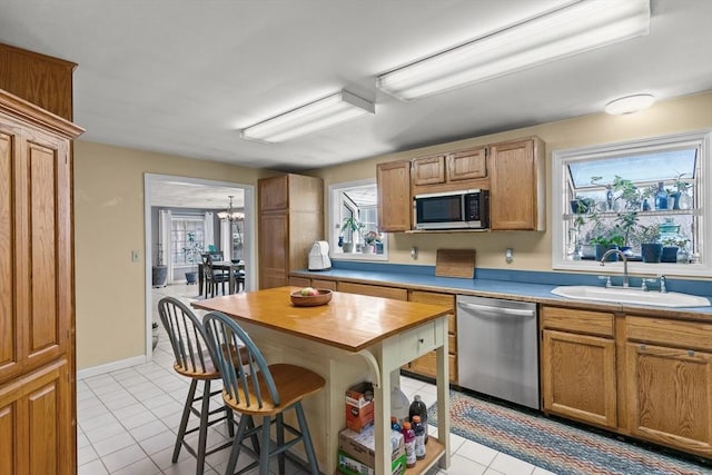 kitchen featuring baseboards, light tile patterned floors, a kitchen breakfast bar, stainless steel appliances, and a sink