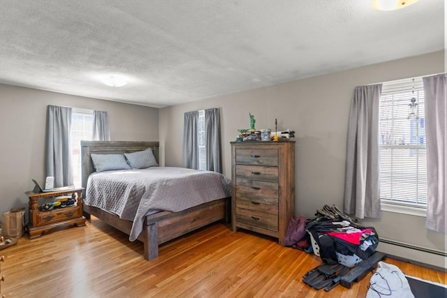 bedroom featuring a baseboard heating unit, light wood-style flooring, and multiple windows