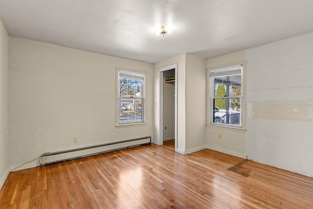 unfurnished bedroom featuring light wood finished floors, baseboard heating, and multiple windows