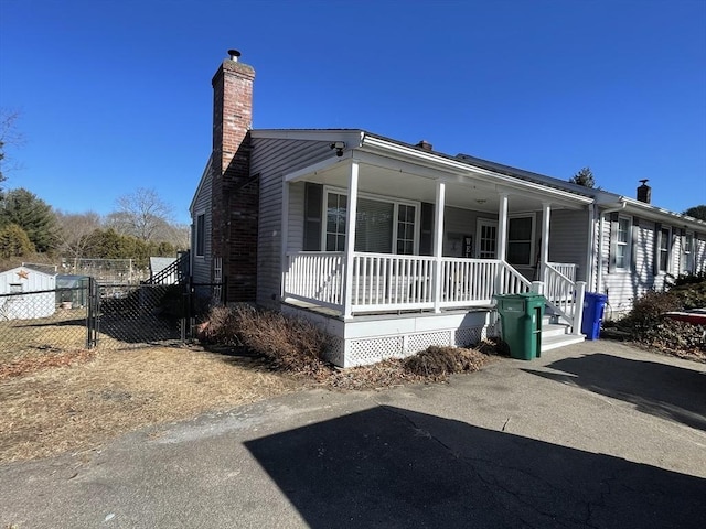 view of front facade featuring a porch, a chimney, and fence