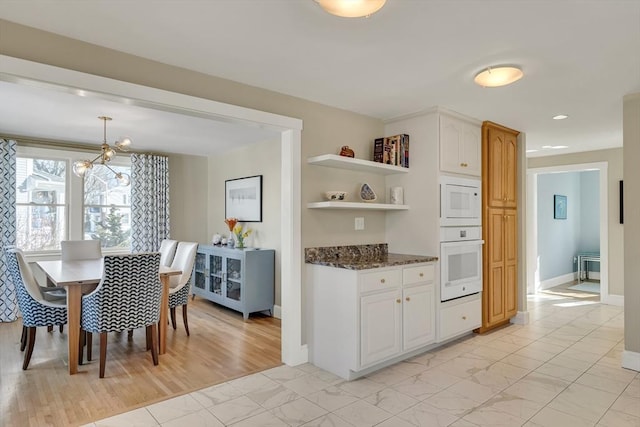 kitchen with an inviting chandelier, white cabinetry, dark stone countertops, and white appliances