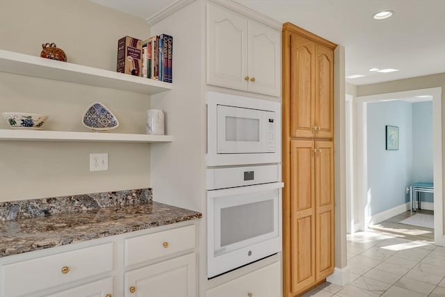 kitchen with dark stone countertops, white cabinets, and white appliances