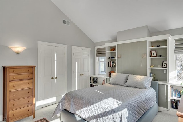 bedroom with light carpet, two closets, and high vaulted ceiling