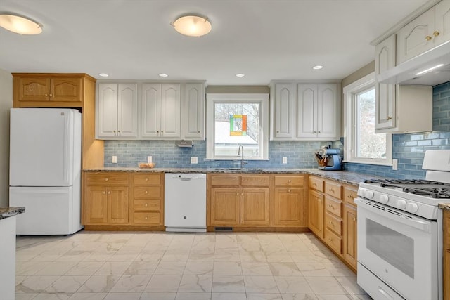 kitchen featuring sink, decorative backsplash, light stone counters, light brown cabinets, and white appliances