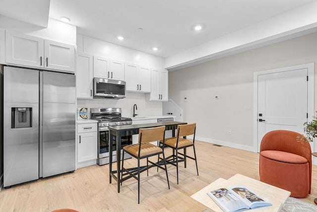 kitchen with white cabinetry, sink, decorative backsplash, appliances with stainless steel finishes, and light wood-type flooring