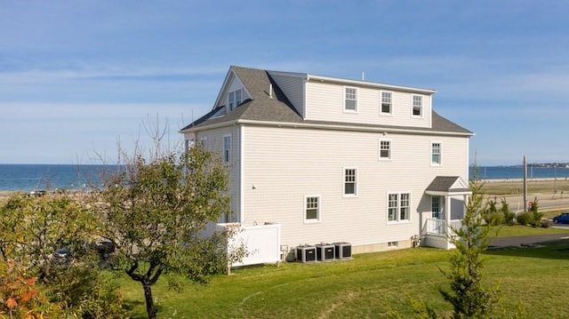 rear view of house with central AC unit, a lawn, and a water view