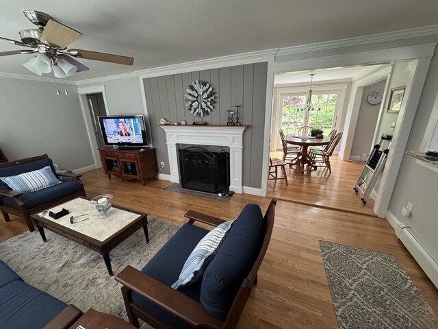living room with ornamental molding, light wood-type flooring, ceiling fan, a baseboard heating unit, and baseboards