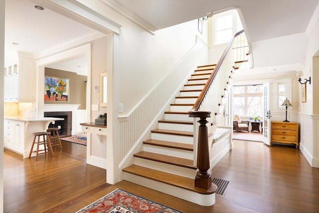 stairs with hardwood / wood-style floors, ornamental molding, and a brick fireplace