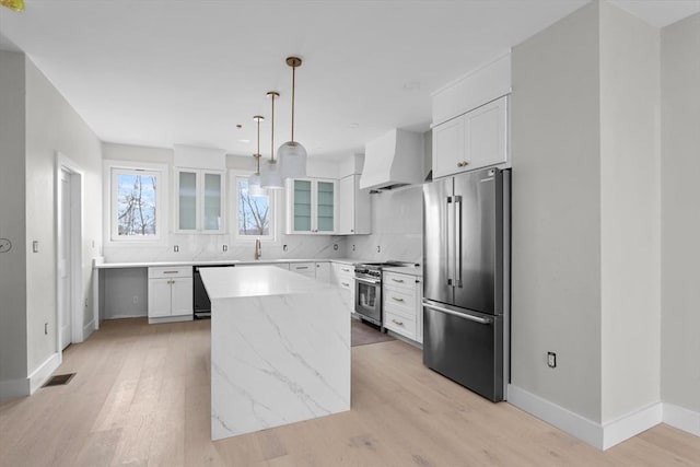 kitchen featuring premium appliances, wall chimney range hood, a kitchen island, white cabinets, and pendant lighting