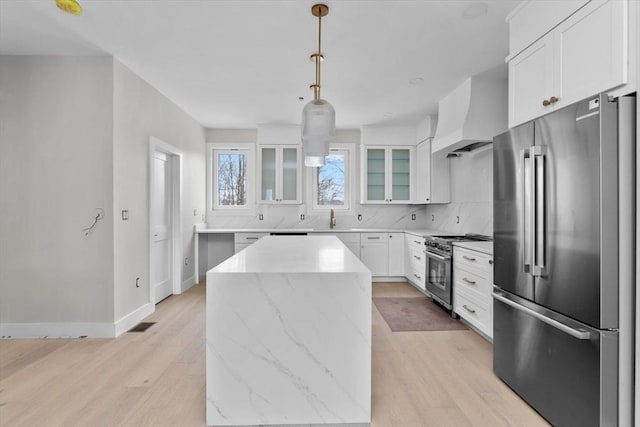 kitchen featuring a center island, premium range hood, white cabinetry, pendant lighting, and high quality appliances