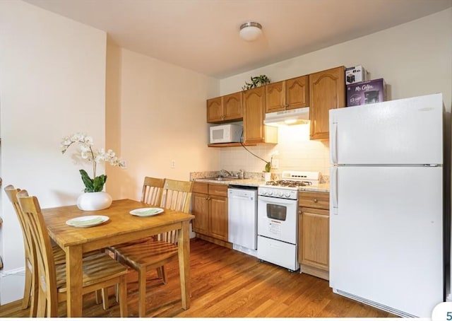 kitchen with white appliances, under cabinet range hood, light countertops, decorative backsplash, and wood finished floors