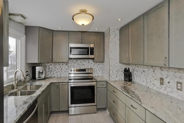 kitchen with stainless steel appliances, sink, light stone counters, and decorative backsplash