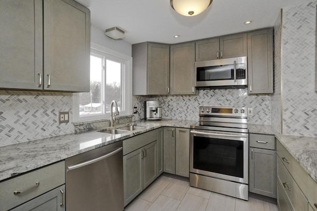 kitchen with appliances with stainless steel finishes, gray cabinets, light stone countertops, and sink