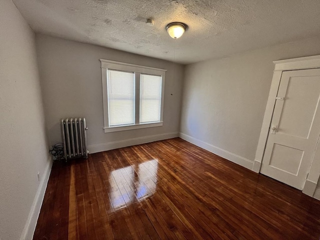 empty room featuring radiator, wood-type flooring, and baseboards