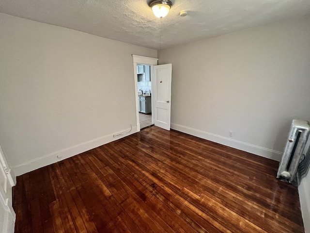 unfurnished bedroom with dark wood-style flooring, baseboards, a textured ceiling, and radiator heating unit