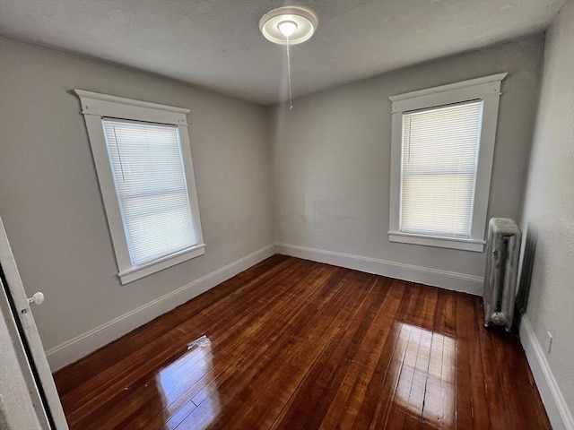 unfurnished room featuring baseboards, a healthy amount of sunlight, hardwood / wood-style flooring, and radiator