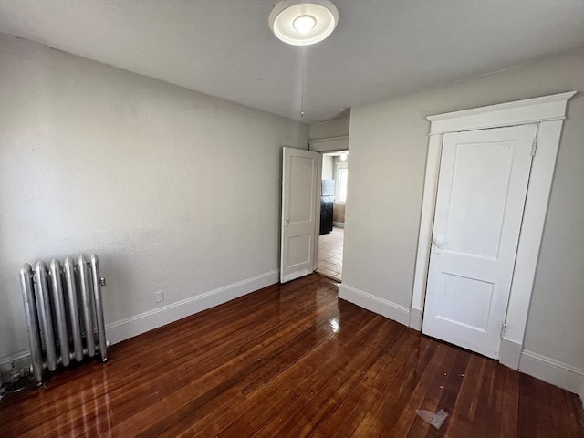 unfurnished bedroom featuring freestanding refrigerator, radiator, baseboards, and hardwood / wood-style flooring