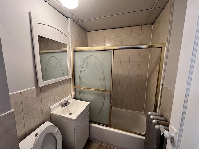 full bathroom with radiator, toilet, enclosed tub / shower combo, vanity, and tile walls