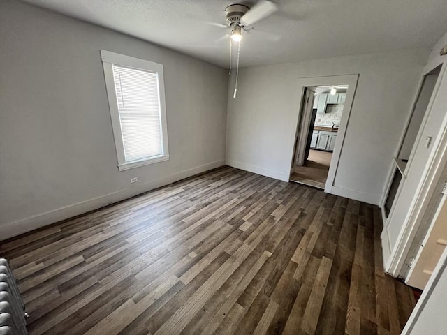 unfurnished bedroom featuring dark wood-style floors, radiator heating unit, ceiling fan, and baseboards