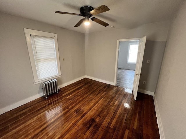 spare room featuring radiator, baseboards, ceiling fan, and dark wood-style flooring