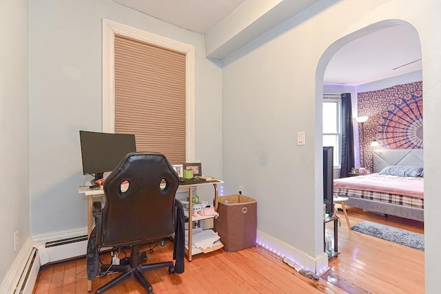 office area with arched walkways, a baseboard heating unit, baseboards, and hardwood / wood-style flooring