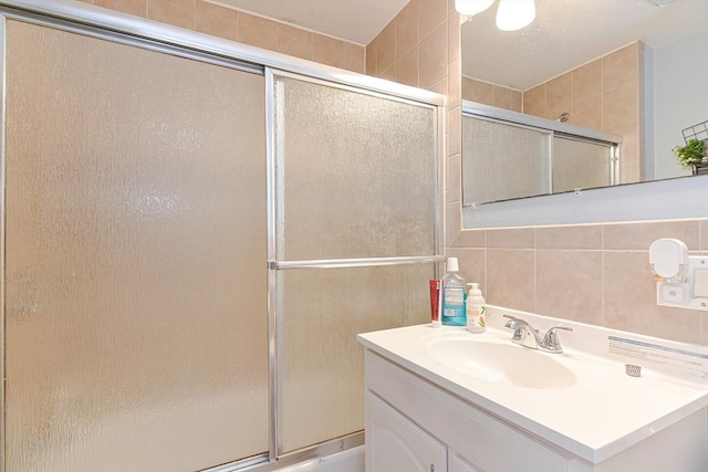 full bathroom featuring a shower with door, tile walls, and vanity