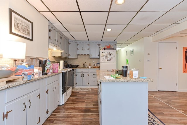 kitchen with white appliances, wood finished floors, under cabinet range hood, backsplash, and a center island