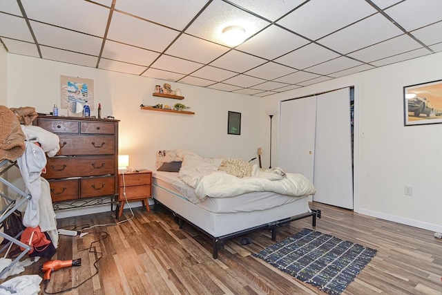 bedroom featuring a closet, a paneled ceiling, baseboards, and wood finished floors