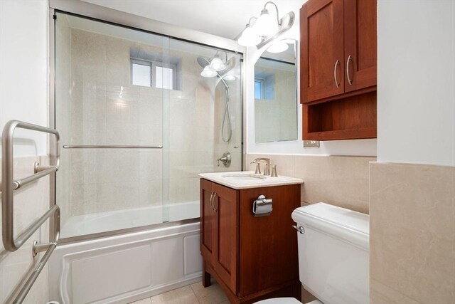 full bathroom featuring shower / bath combination with glass door, vanity, tile patterned floors, tile walls, and toilet