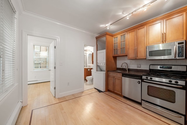 kitchen with appliances with stainless steel finishes, backsplash, sink, stacked washer and dryer, and baseboard heating