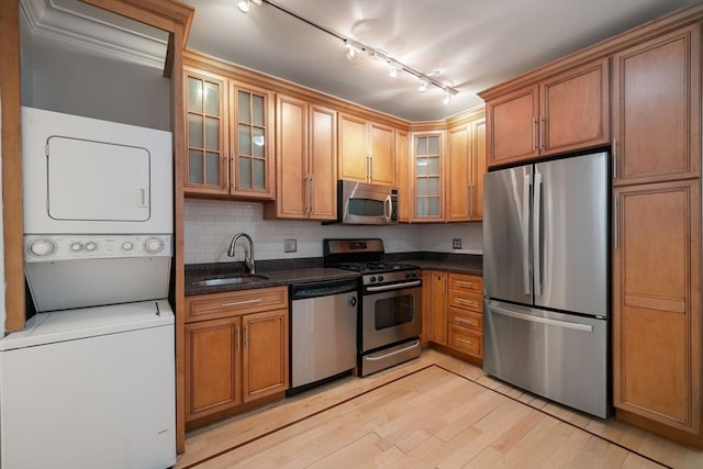 kitchen featuring stainless steel appliances, light hardwood / wood-style floors, stacked washing maching and dryer, rail lighting, and sink