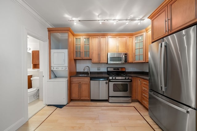 kitchen featuring appliances with stainless steel finishes, light hardwood / wood-style flooring, ornamental molding, sink, and stacked washer / dryer