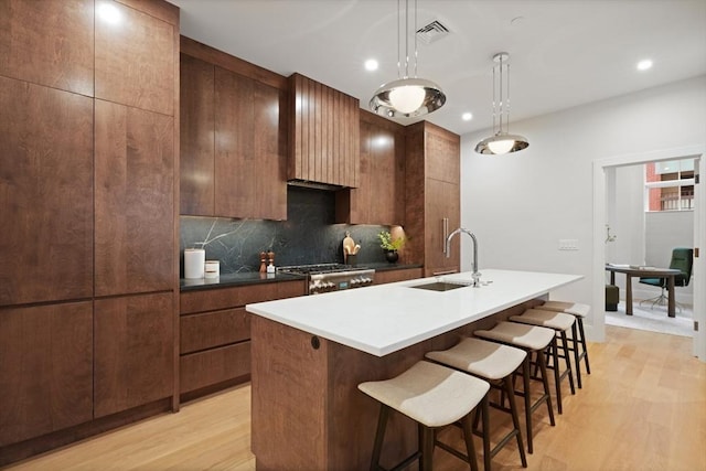 kitchen featuring a sink, decorative backsplash, light wood finished floors, and visible vents