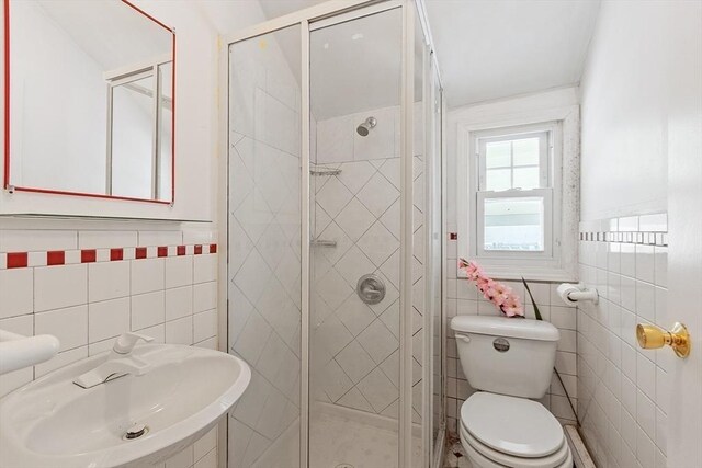 full bath featuring toilet, a stall shower, tile walls, and a sink