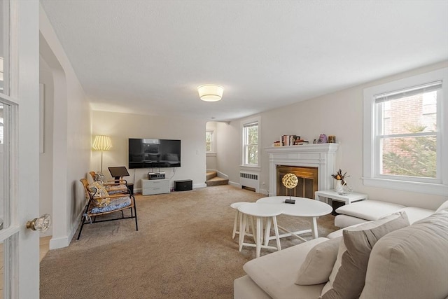 living room featuring a fireplace, radiator, carpet flooring, baseboards, and stairs