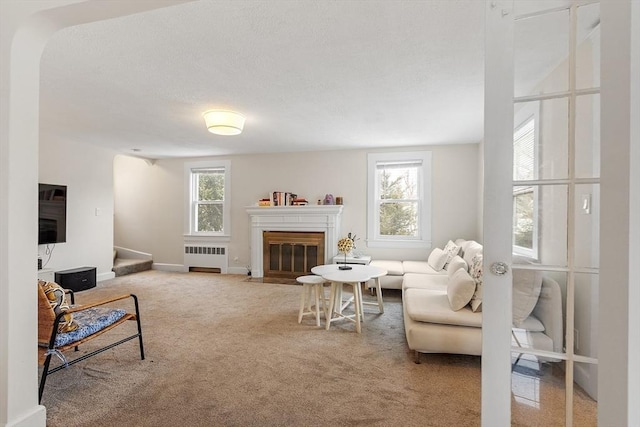 living room with carpet flooring, a fireplace with flush hearth, baseboards, stairway, and radiator heating unit