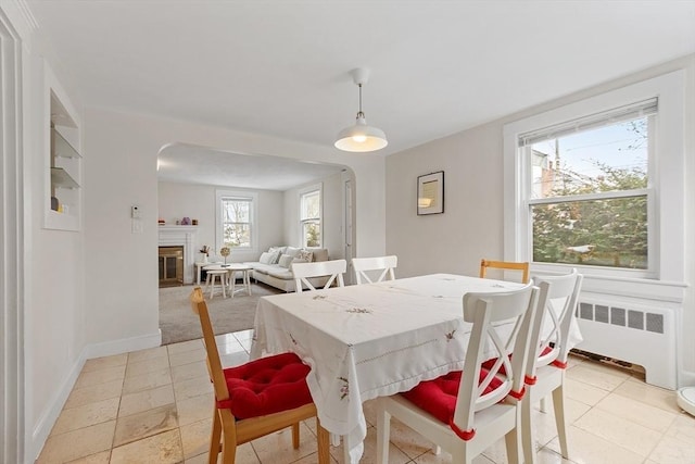 dining space featuring radiator heating unit, baseboards, arched walkways, and a glass covered fireplace