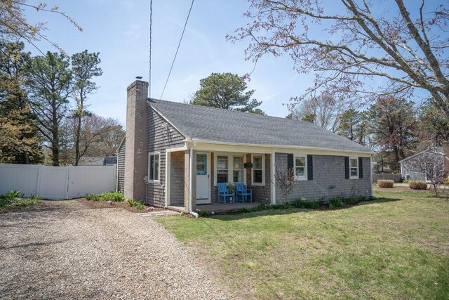 view of side of home with fence, a chimney, covered porch, a yard, and gravel driveway