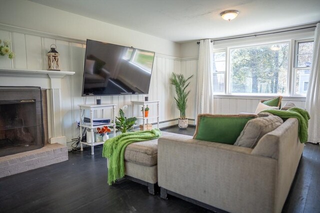 living room with a decorative wall, a brick fireplace, a baseboard heating unit, and dark wood-style floors
