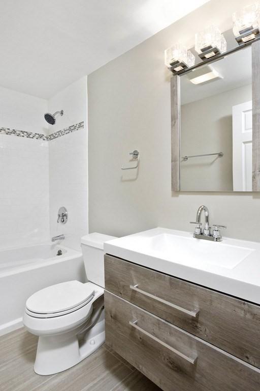 bathroom with toilet, wood finished floors, vanity, and  shower combination