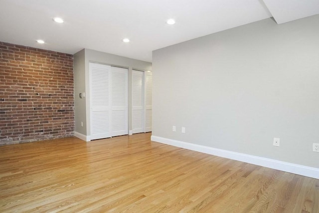 unfurnished bedroom with light wood-style flooring, recessed lighting, baseboards, brick wall, and two closets