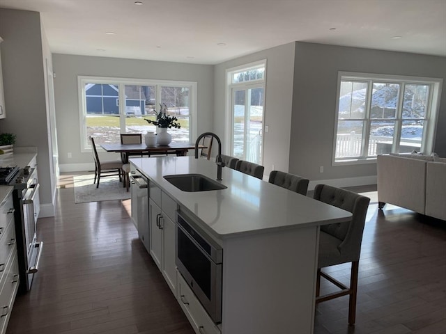 kitchen featuring sink, stainless steel appliances, white cabinetry, a center island with sink, and a breakfast bar