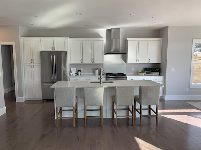 kitchen with white cabinets, wall chimney exhaust hood, a kitchen bar, an island with sink, and stainless steel fridge