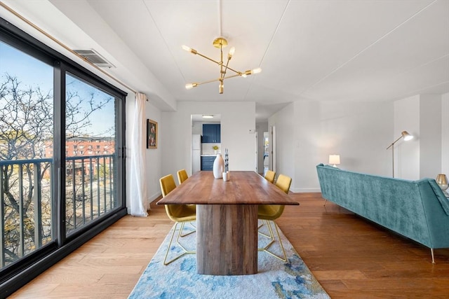 dining space with hardwood / wood-style floors, plenty of natural light, and an inviting chandelier