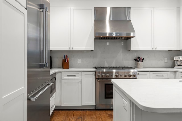 kitchen featuring wall chimney range hood, premium appliances, dark wood-type flooring, decorative backsplash, and white cabinetry