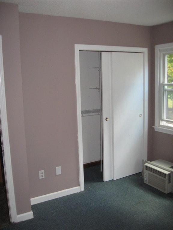 unfurnished bedroom featuring a wall mounted air conditioner, dark carpet, and a closet