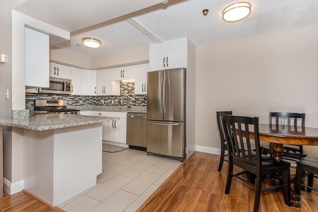 kitchen with light stone counters, a peninsula, appliances with stainless steel finishes, white cabinetry, and backsplash