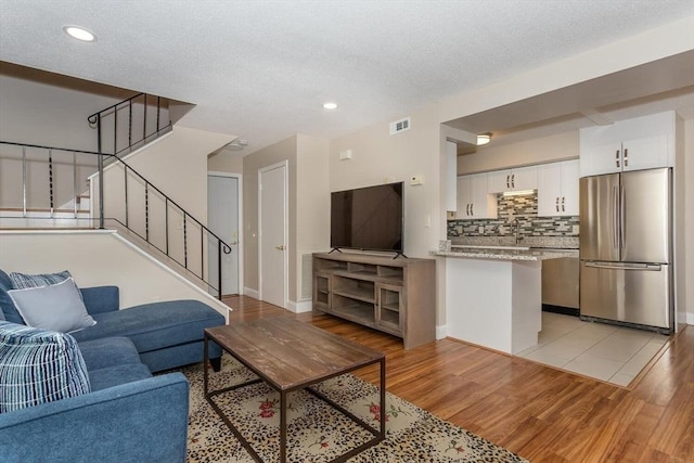 living room with visible vents, light wood-style flooring, a textured ceiling, stairway, and baseboards