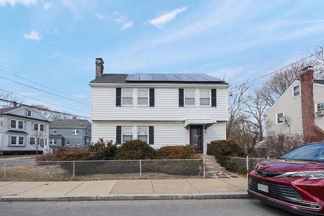 view of front of property featuring a fenced front yard, roof mounted solar panels, and a chimney